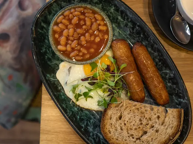 A full breakfast on a dark plate: sausage, bacon, beans, egg and potato scone