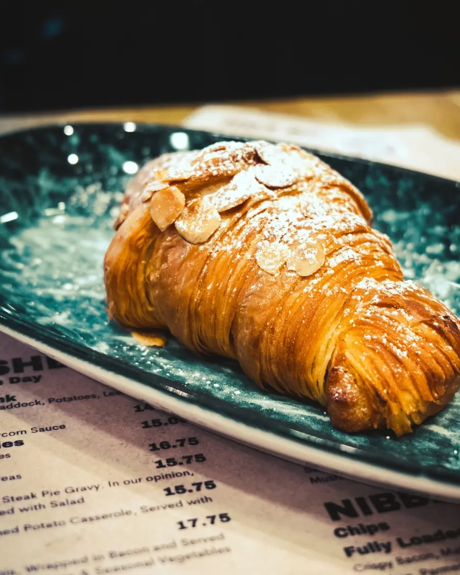 A butter croissant on a dark plate, resting on the printed menu