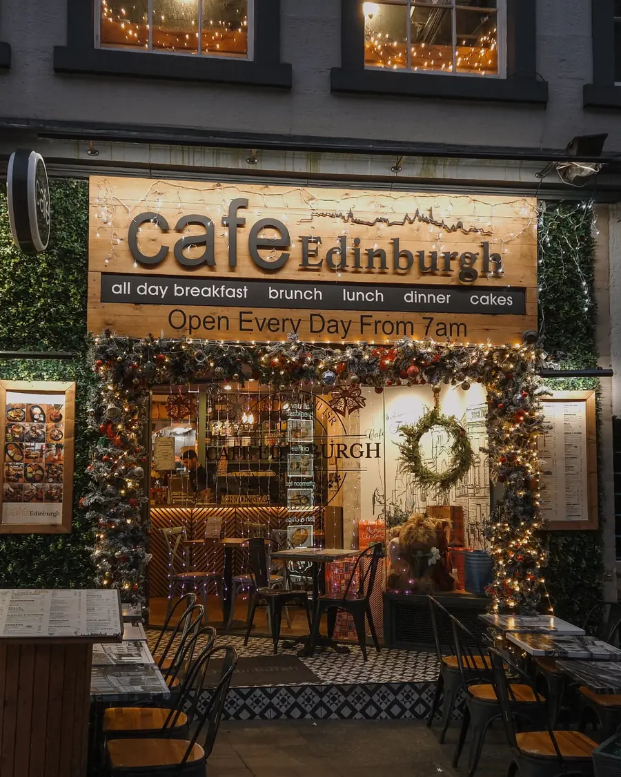 The cafe frontage at dusk, lit up with plants either side of the doorway