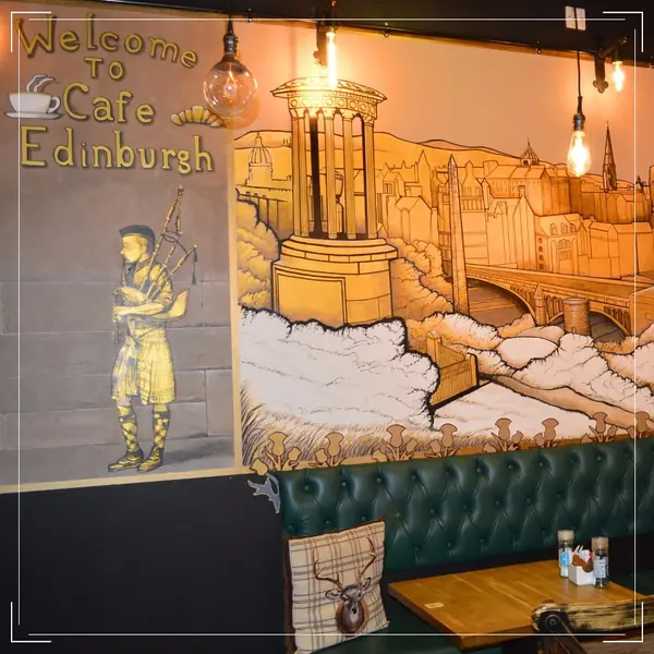 A painted mural above green bench seating under a row of warm wall lights
