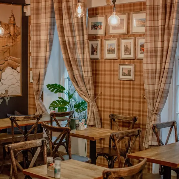 Bare wooden tables and chairs under plaid curtains and rows of framed prints