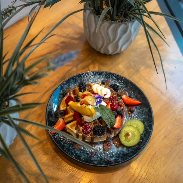 A dark plate of salad with whipped feta, tomato and rocket on a wooden table