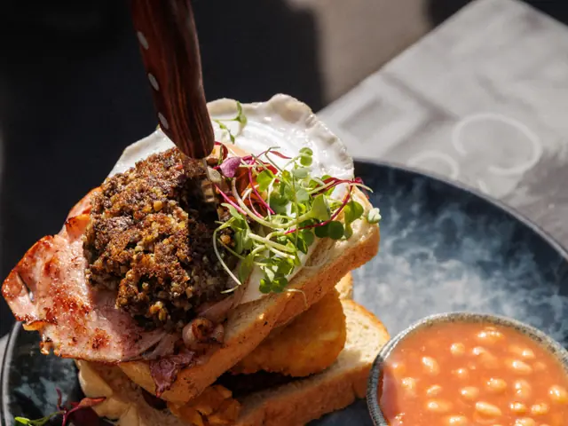 A stacked toasted sandwich on a dark plate with a pot of sauce